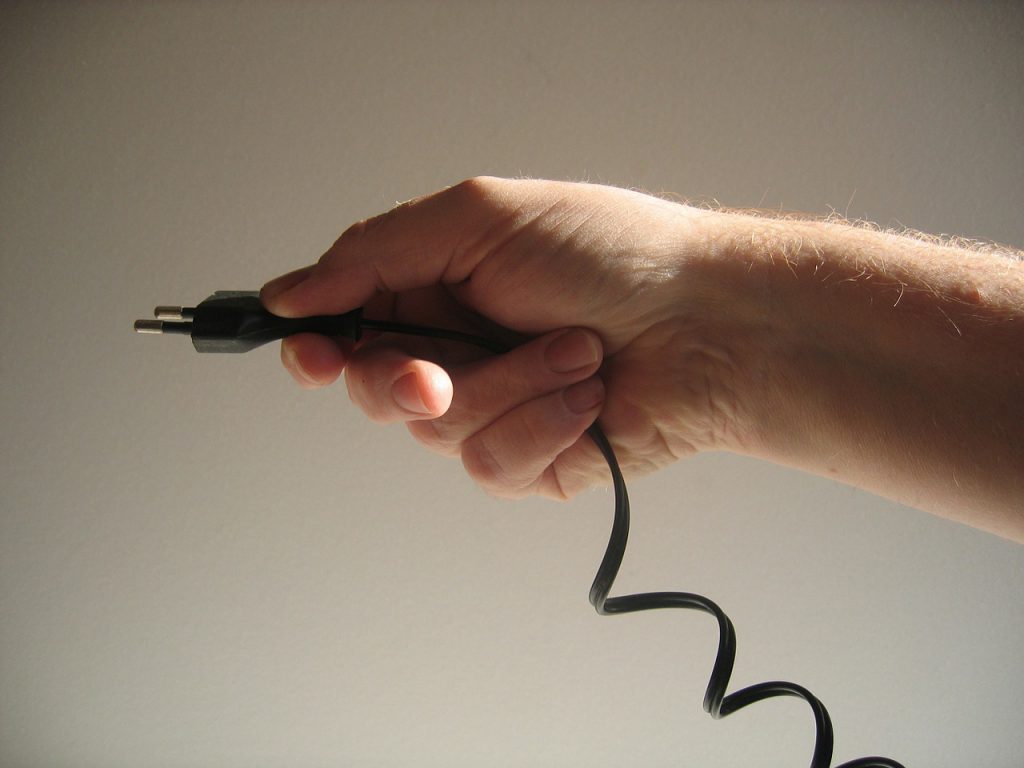 Imagem de uma mão segurando um fio de energia, sob um fundo claro.