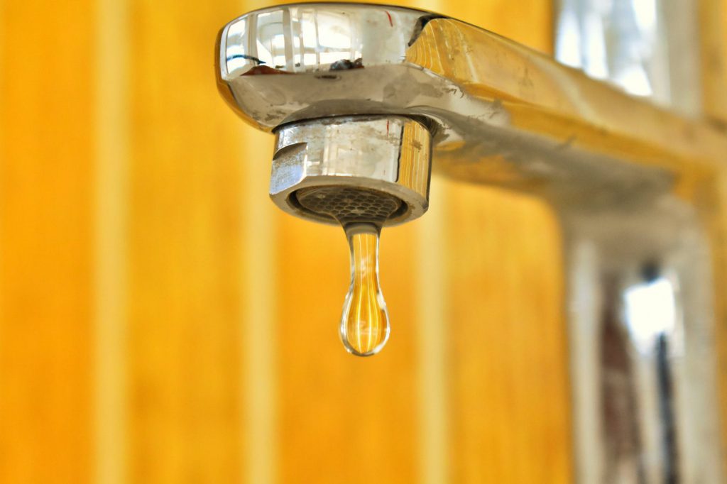 Uma das dicas de como preservar o meio ambiente é economia de água, por isso a imagem de close-up de uma torneira liberando uma gota d’água. 