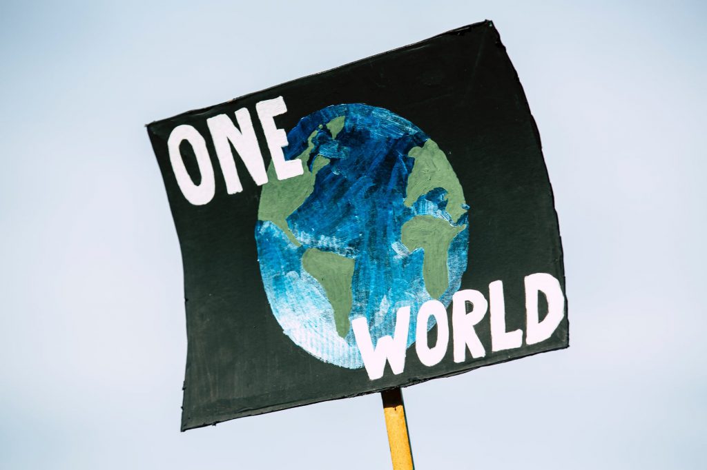 Imagem mostra um cartaz de ativismo climático, nele tem a imagem do planeta Terra e diz “um mundo”.