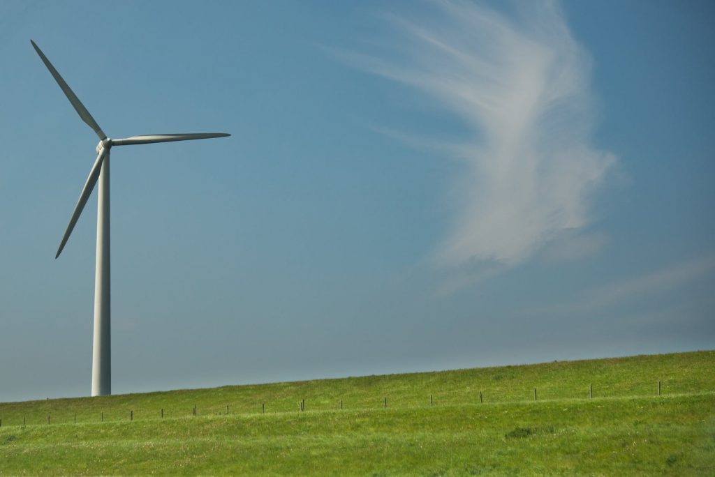 A imagem mostra uma turbina eólica localizada em ambiente externo, em um vasto gramado, com o céu ao fundo.