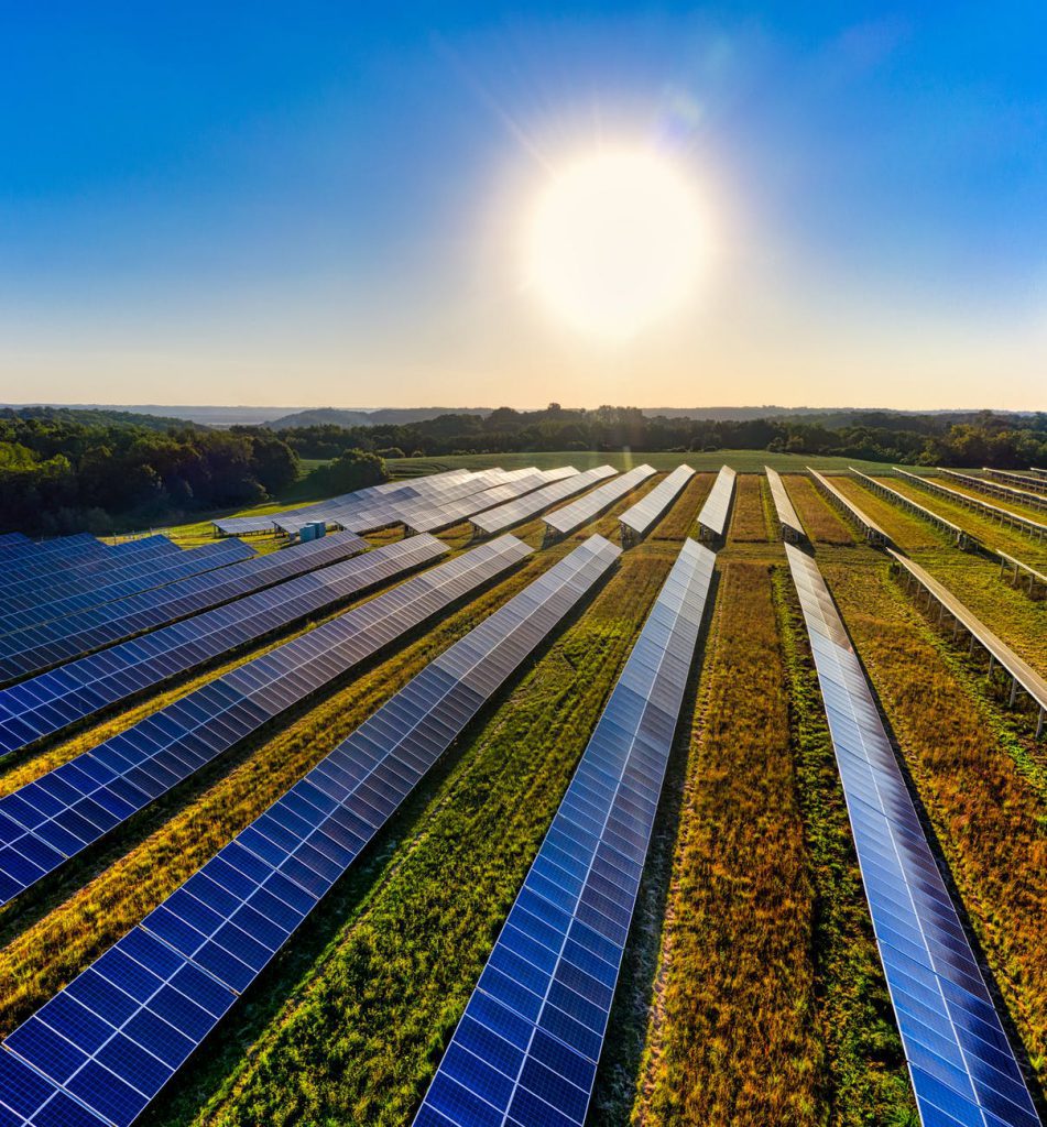 Vista aérea de painéis de energia solar, que é um exemplo de energias verdes, localizado em ambiente externo, durante o dia, em meio a um gramado.