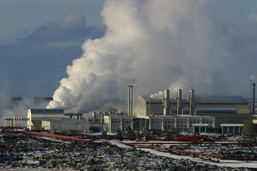 Imagem de uma usina geotérmica, exemplo de energias verdes, com grande liberação de vapor, durante um dia nublado.