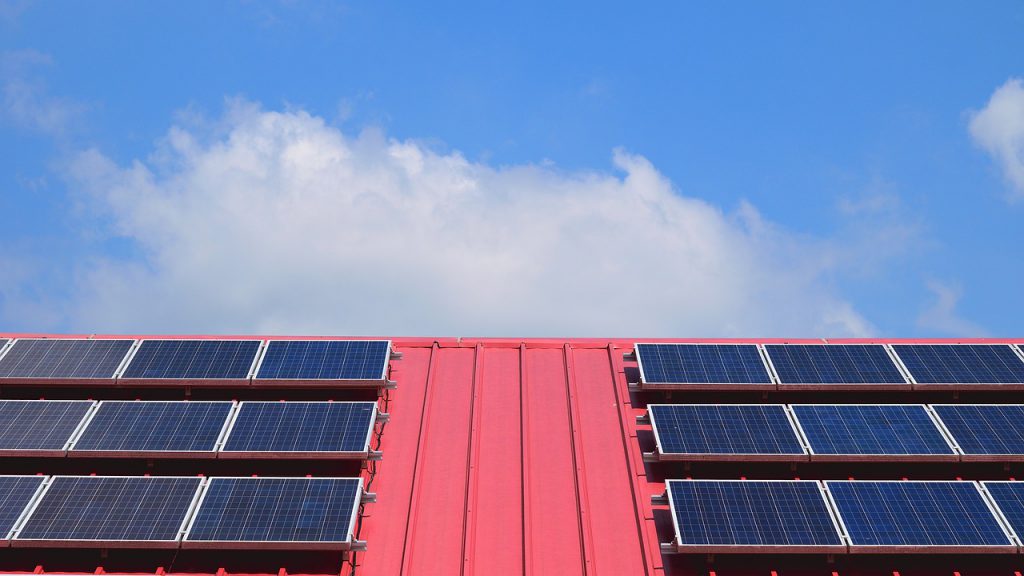 Close-up de um exemplo de geração de energia solar compartilhada, com um telhado com painéis de energia solar sobre ele, e ao fundo, o céu.